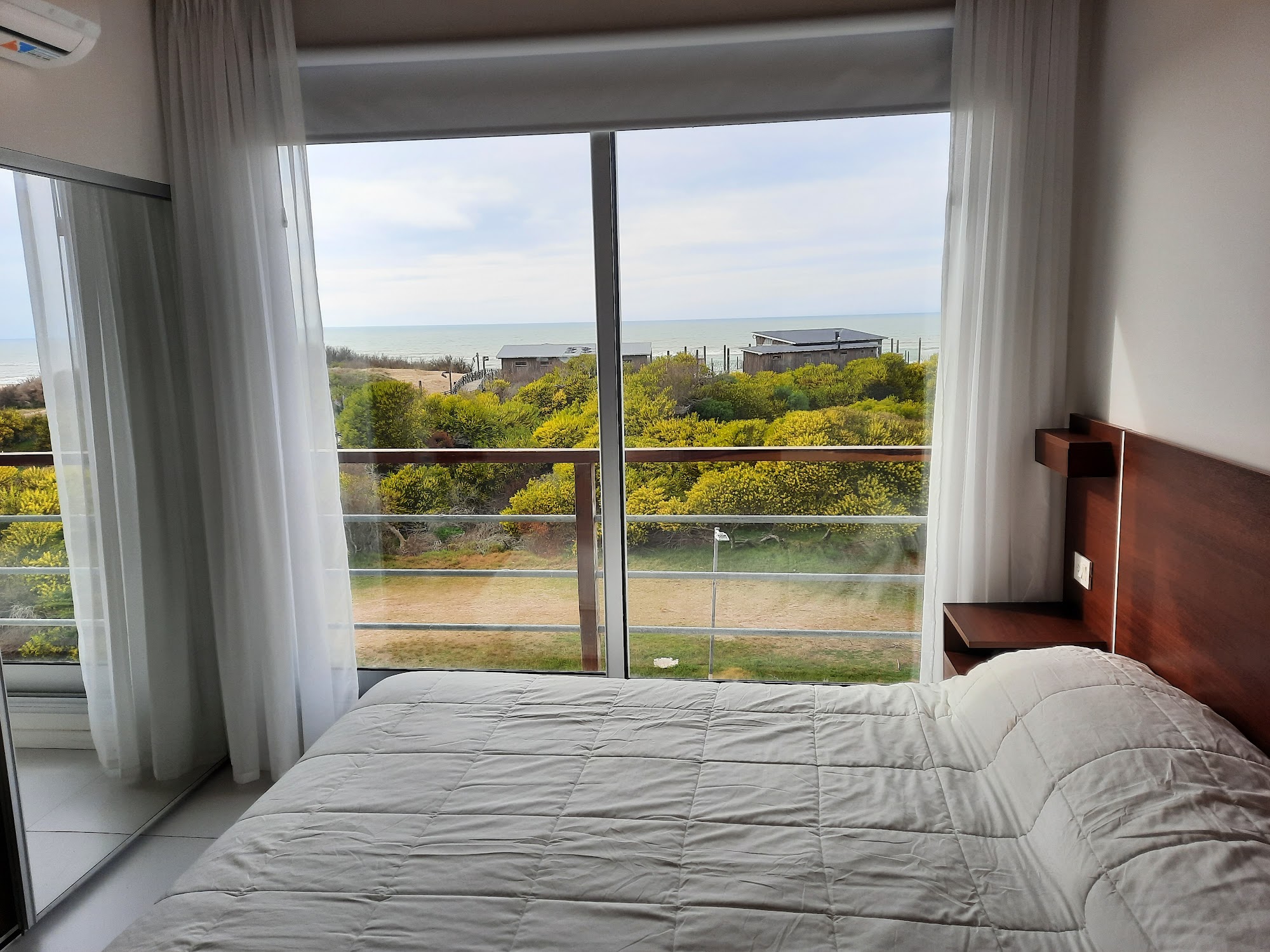 Dormitorio con cama King frente a un ventanal, con los médanos y el mar de fondo.