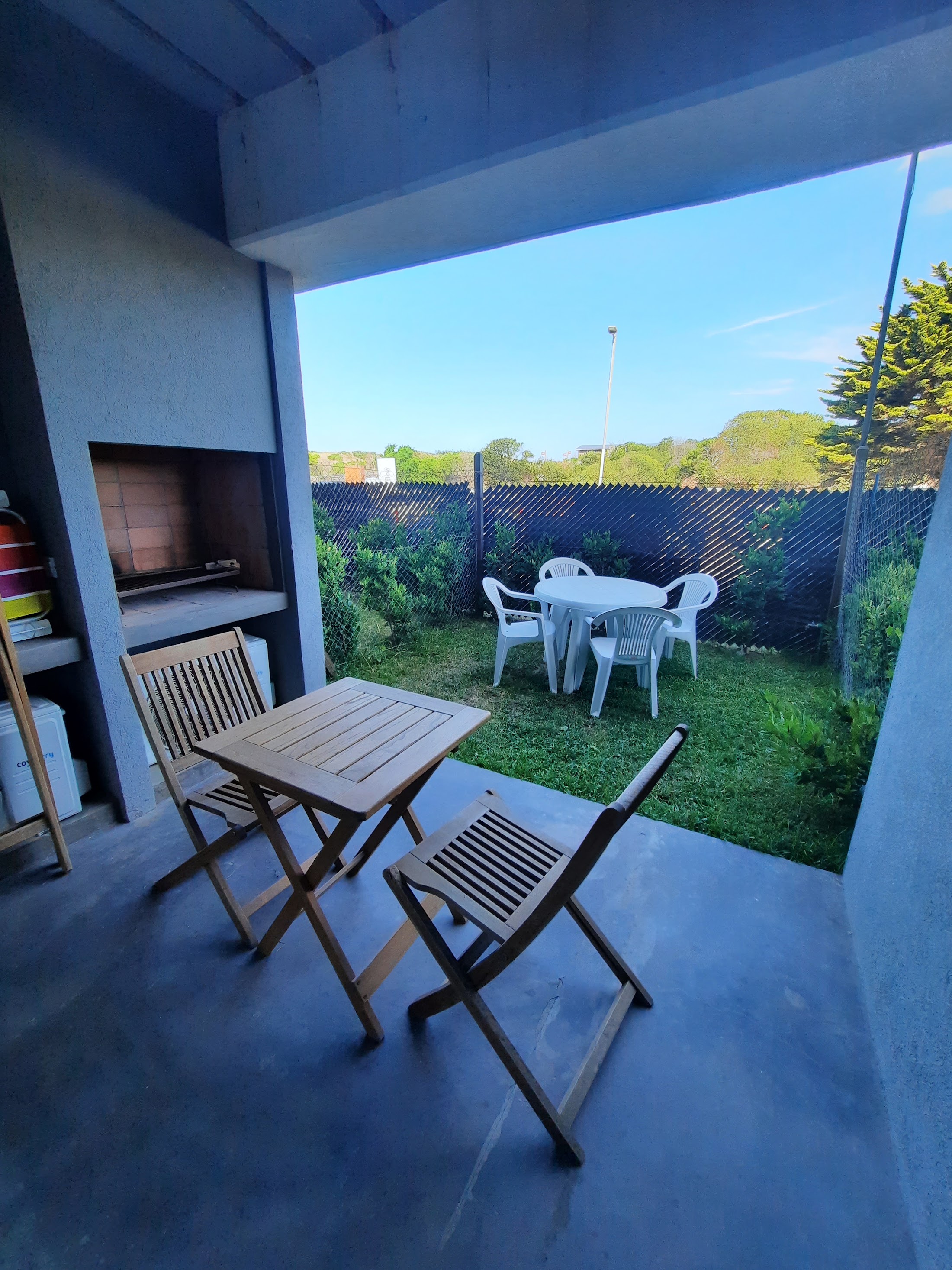 Deck techado con mesa, sillas y parrilla, abierto a un jardín de uso exclusivo.