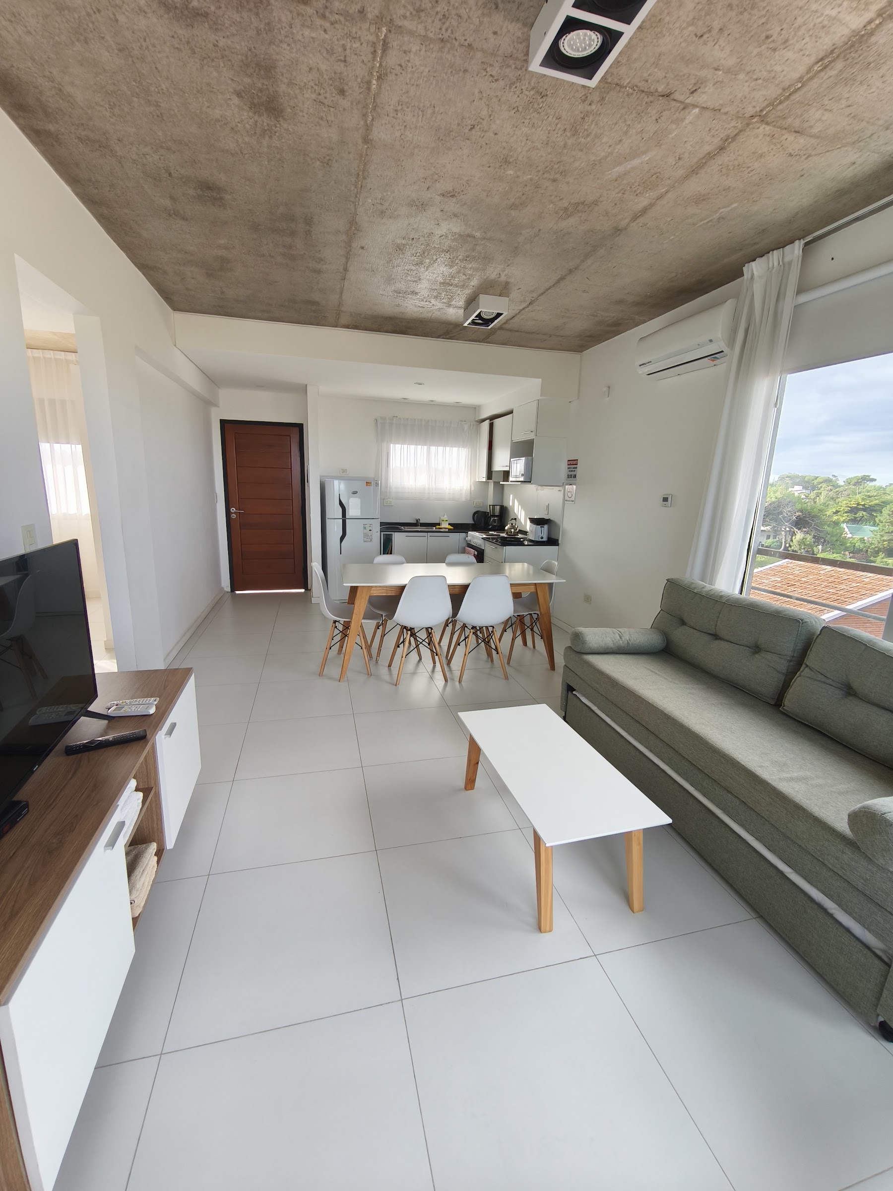 Estar-comedor con sofá, mesa y cocina al fondo.