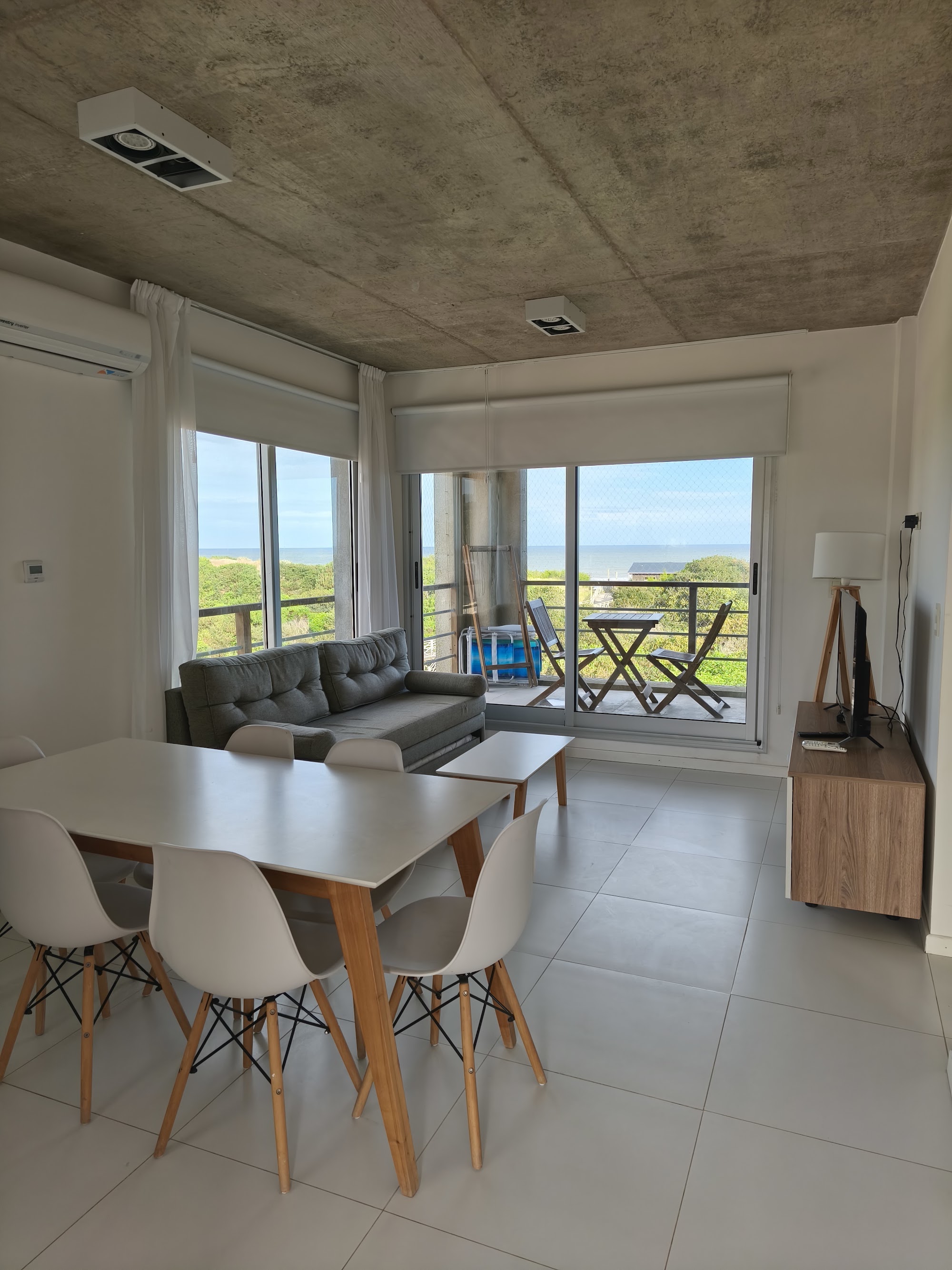 Comedor con mesa para seis y el estar con salida al balcón.