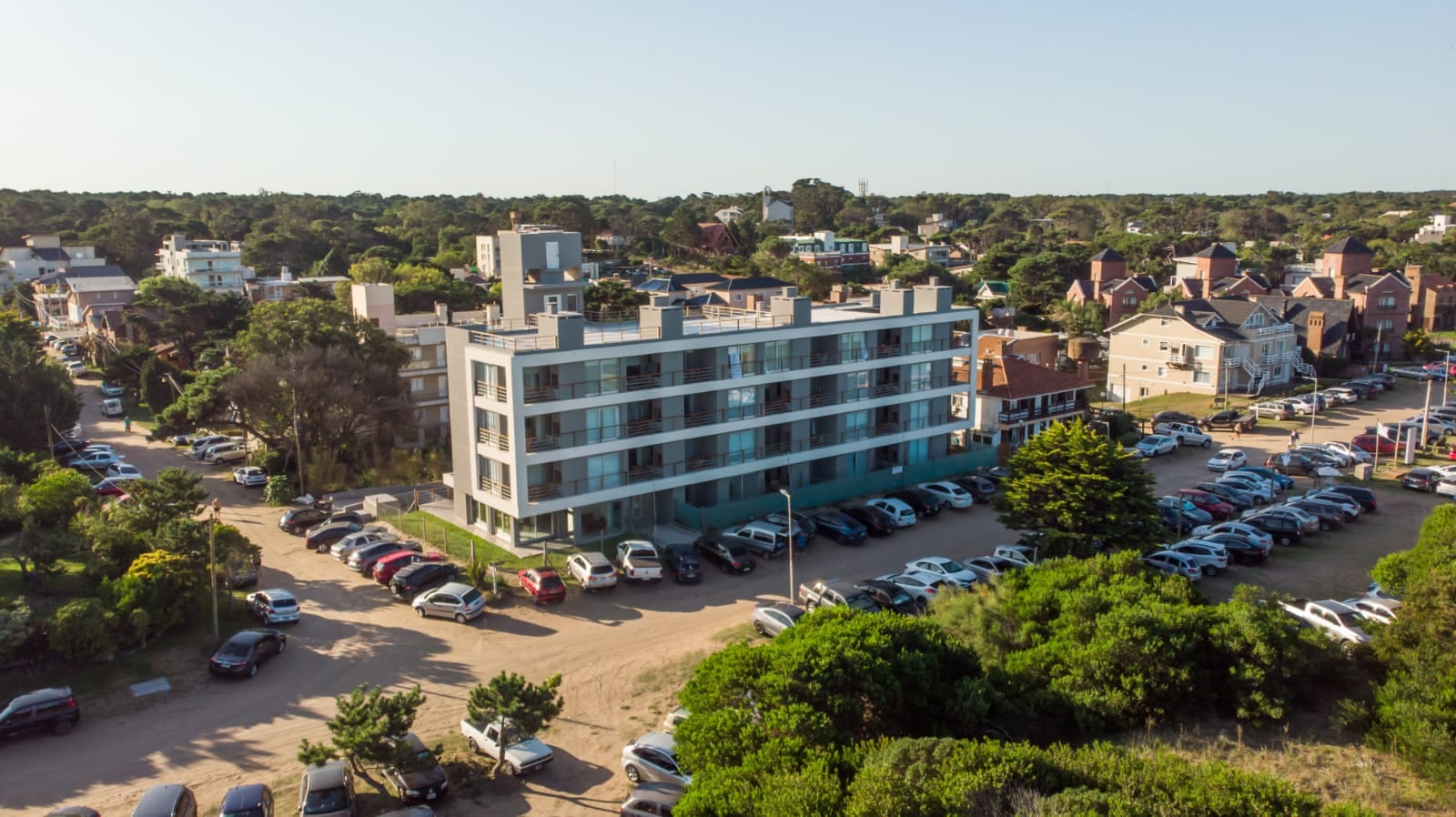 Vista aérea del frente del edificio, sobre la costanera de Valeria del Mar, rodeado de bosque.
