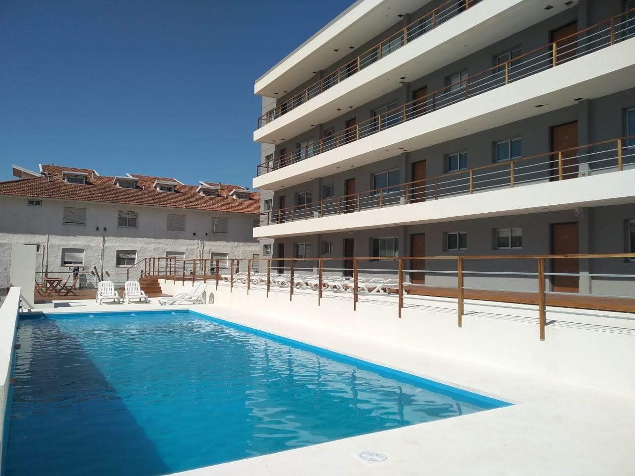La piscina del complejo con el edificio detrás, un mediodía de sol.